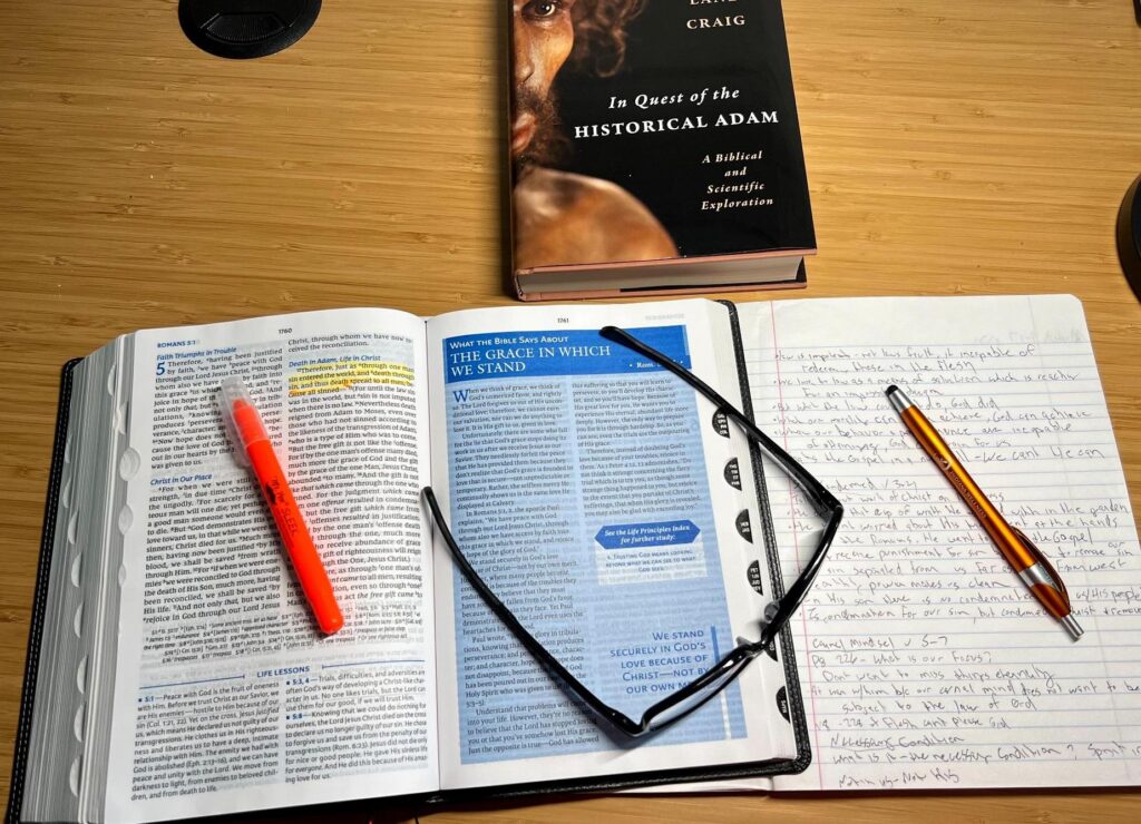 Open Bible with a highlighter and notes beside “In Quest of the Historical Adam” by William Lane Craig